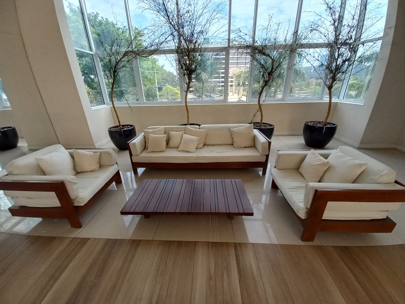 Lobby de condomínio com sofás claros, mesa de centro e plantas